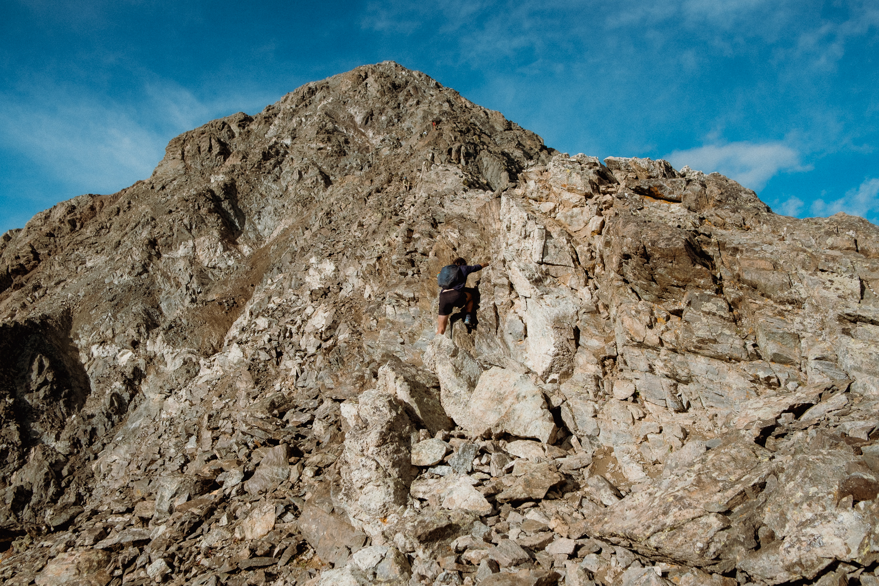 Santo scaling a rocky mountain peak with a blue sky above